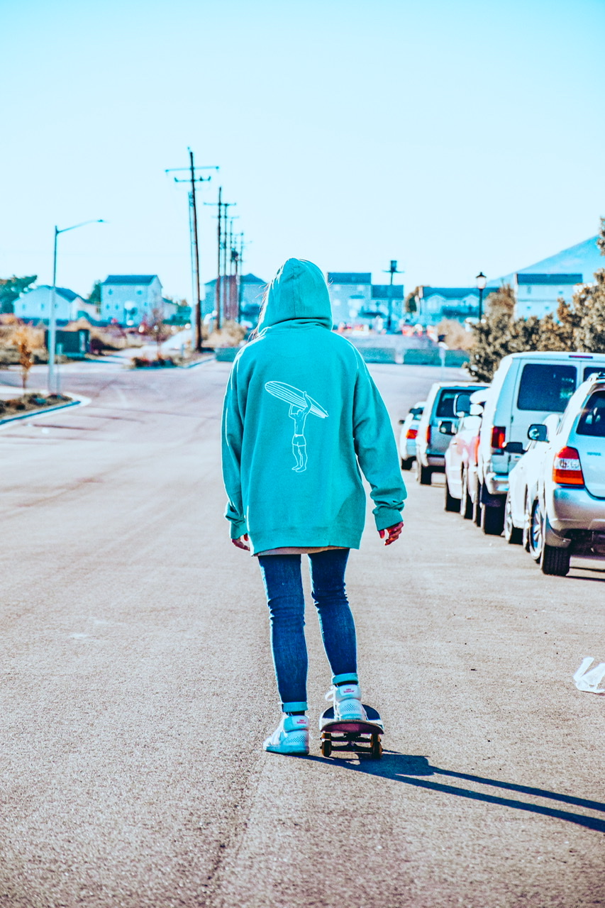 A skateboarder in a street wearing our teal blue headless surfer hoodie.