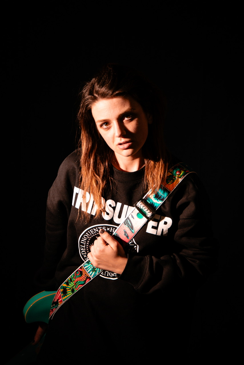 A girl wearing the imperial sweatshirt and holding a guitar with the TripSurfer Comic Book Guitar Strap.